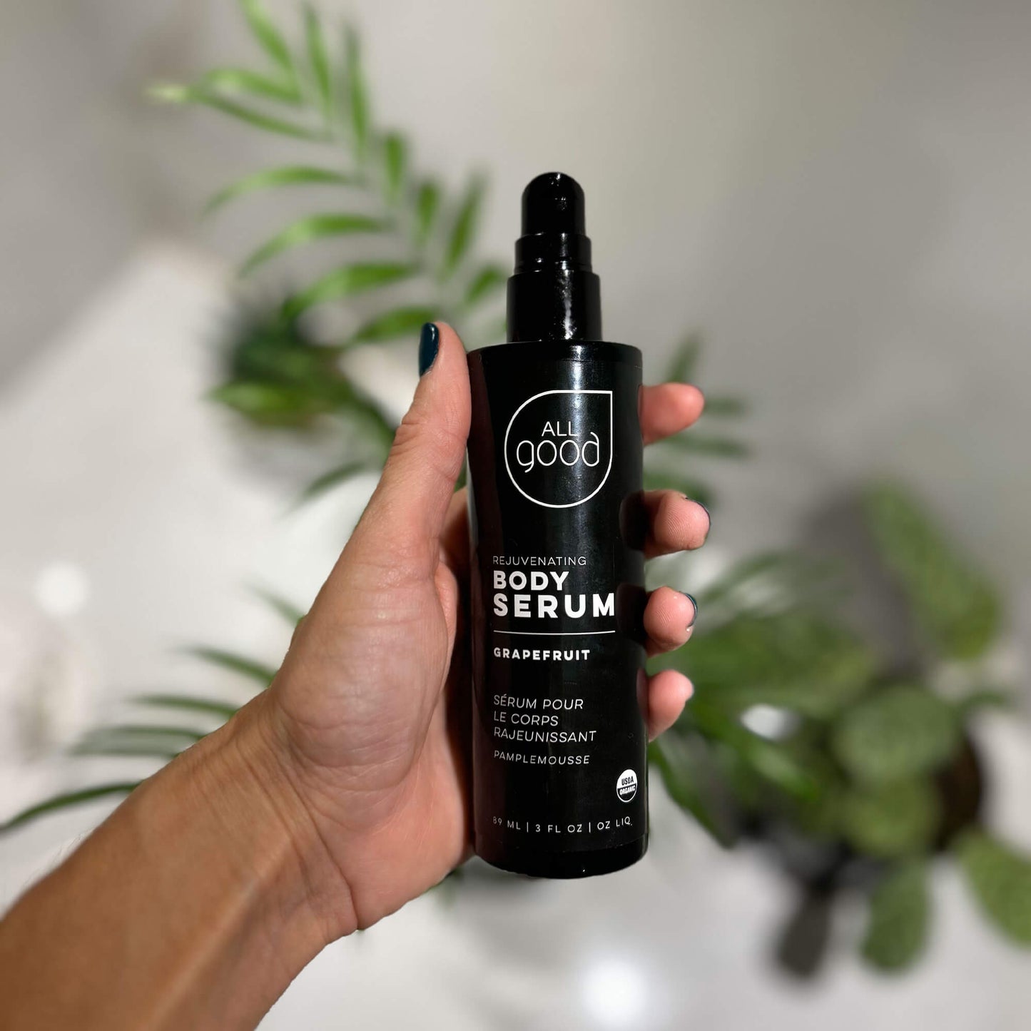 Hand holding All Good Body Care - Rejuvenating Body Serum Grapefruit in their bathroom , 3 fl oz